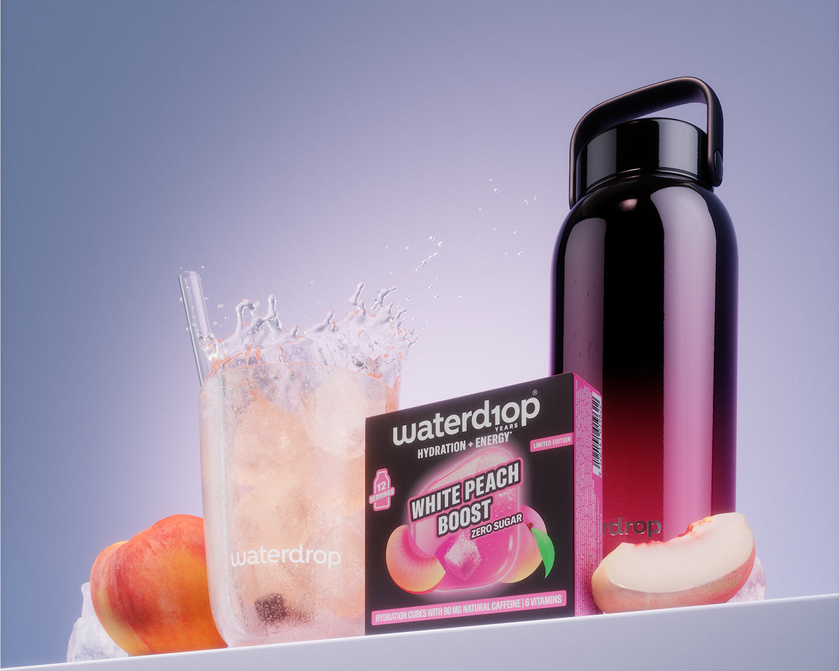Kutija proizvoda White Peach Boost pored čaše ledenog napitka i crne boce na beloj polici.
