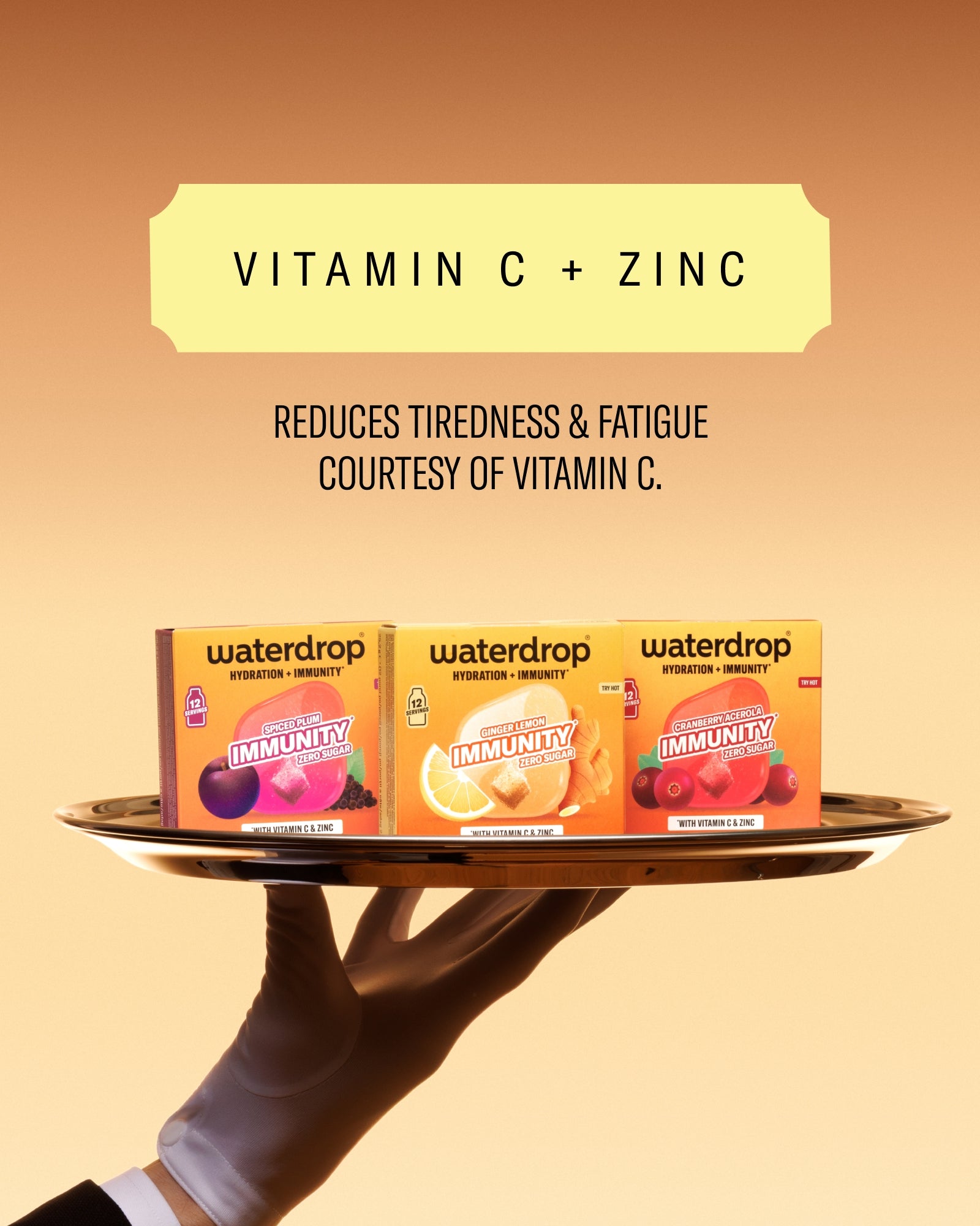Tri kutije vitamina na kružnoj tacni koju drži ruka obučena u rukavici, pozadina narandžaste gradijacije.