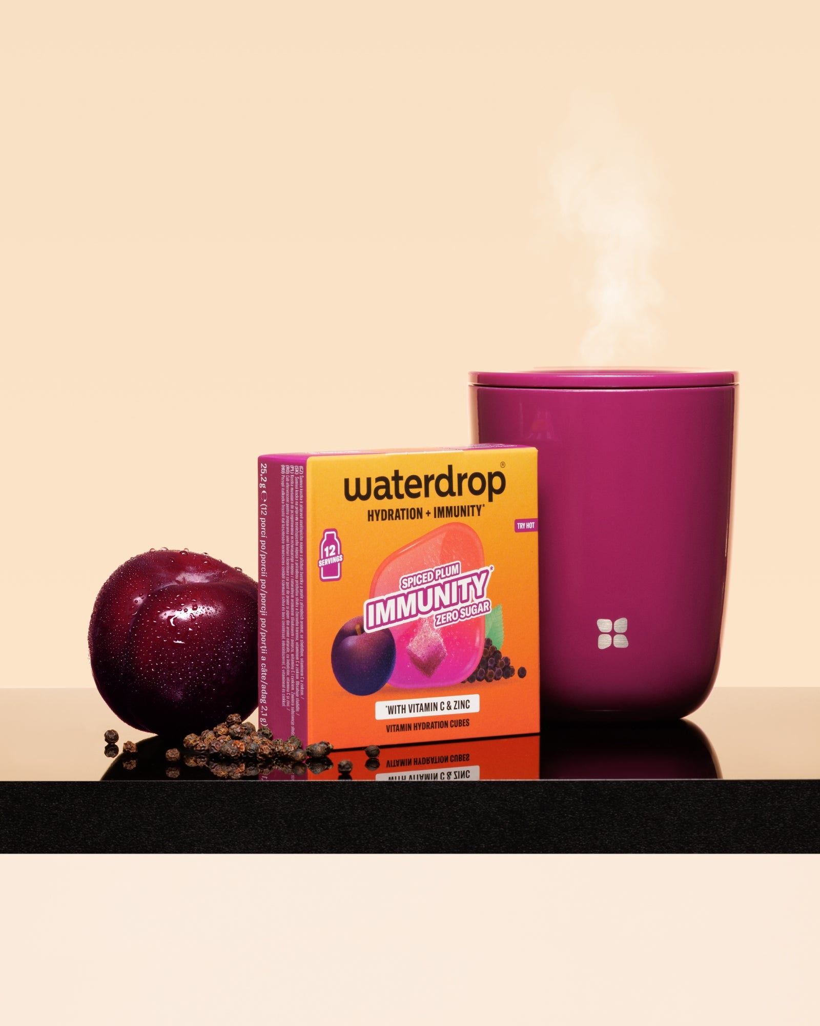 Kutija Waterdrop imunostimulans uz šljivu i ružičastu šolju s parom na crnoj površini.